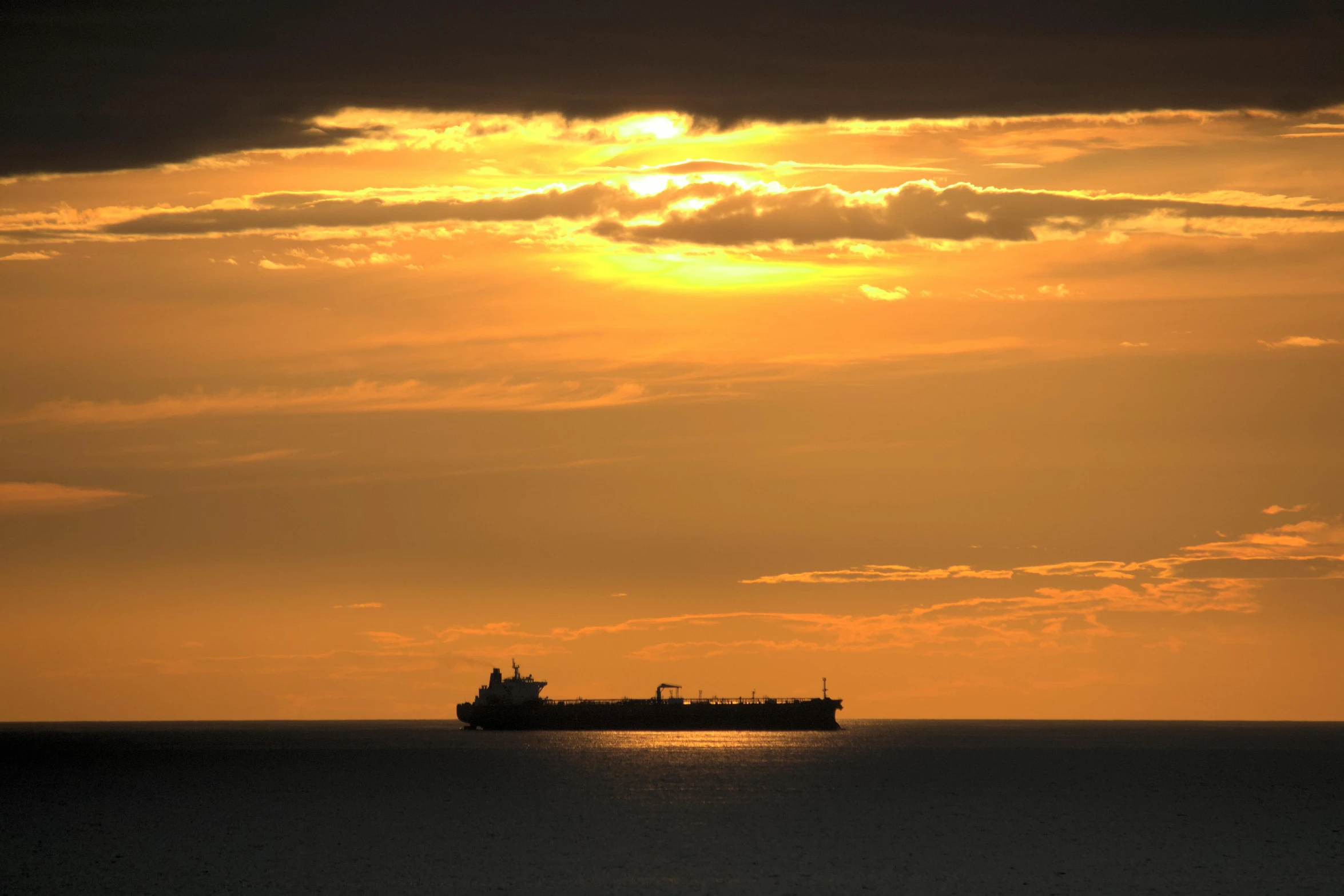 the silhouette of a ship is seen against an orange sky