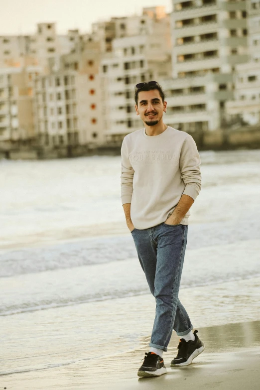 a man in a sweater and jeans stands on the beach