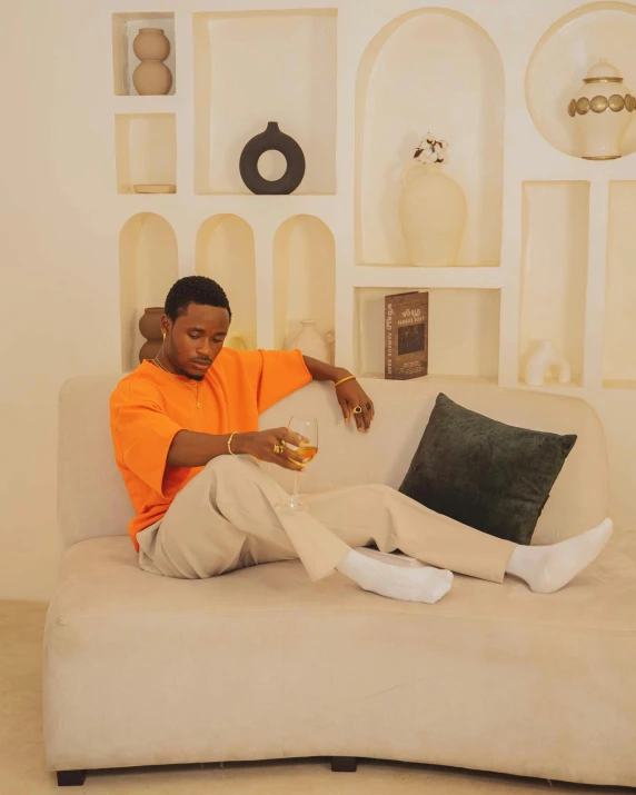 a man in an orange shirt sitting on a white couch with his legs folded out