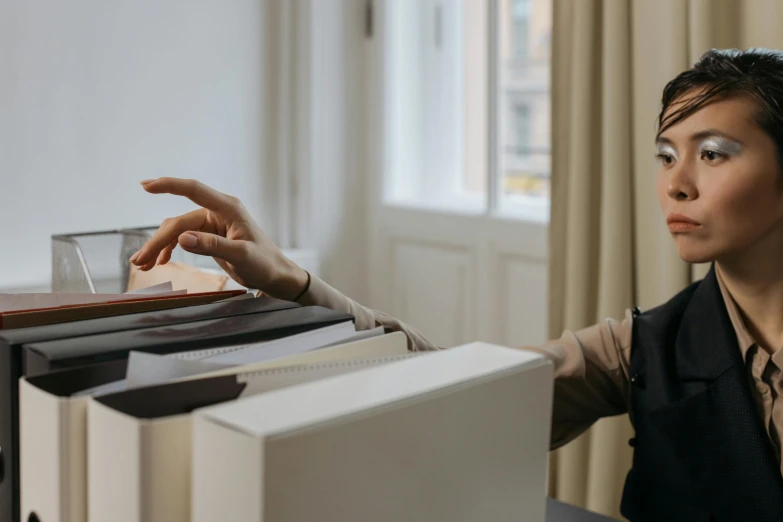 a lady in black dress and shirt sitting by a stack of folders