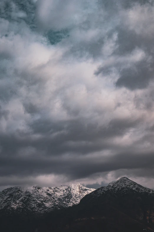 the mountain range is dotted with snow as the cloudy sky looms overhead