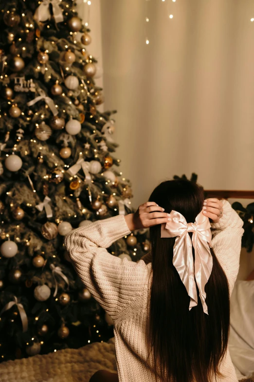 a woman holding a bow while sitting near a christmas tree