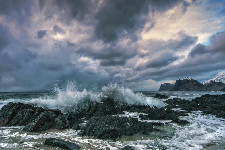 a storm rolls in over the ocean as a large wave crashes on rocks