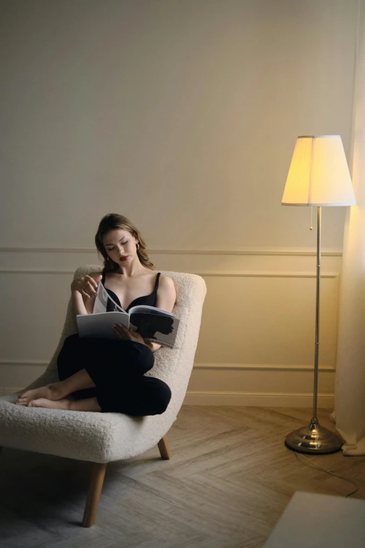 a woman sitting on a white chair next to a lamp