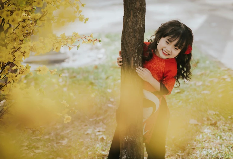 a young child peeking up against the tree