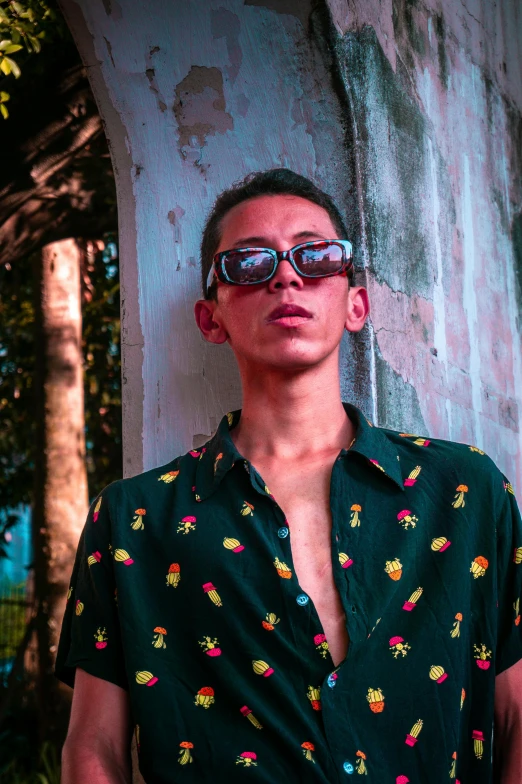 a young man is standing by a tree wearing sunglasses