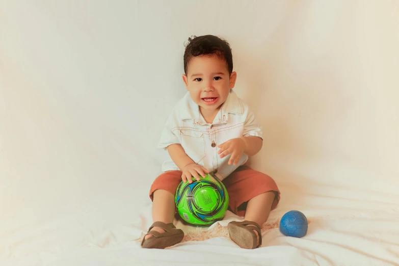 small boy holding a green soccer ball on the ground