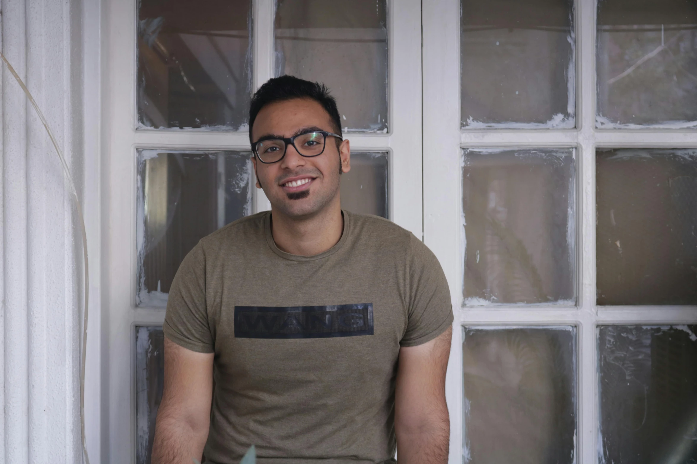 a man with glasses standing next to a window