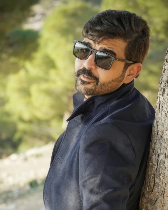 a man leaning up against a tree wearing sunglasses