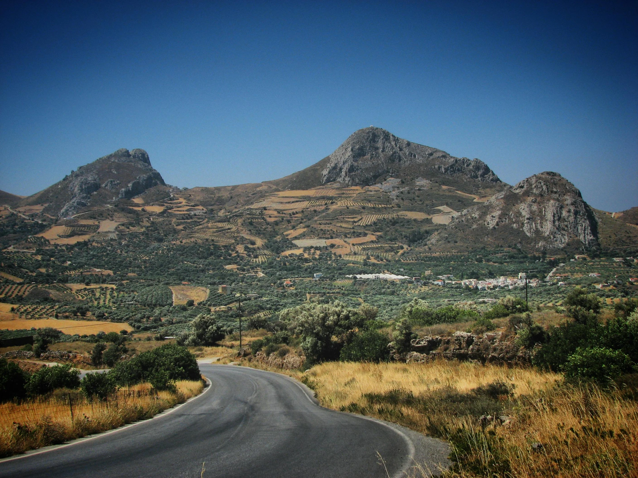 the road runs along a hill - side with tall, grassy hills in the background