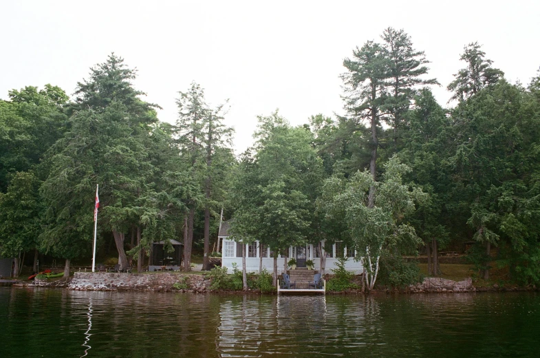 the calm water of the lake is reflected by trees and fence