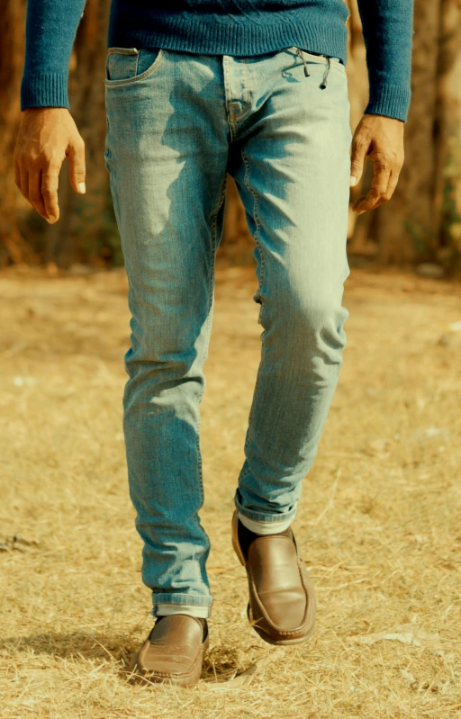 a man in jeans is standing on some dry grass
