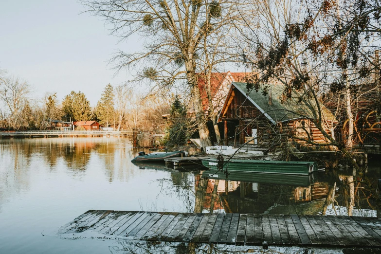 a house is sitting on the side of a lake with some boats and trees