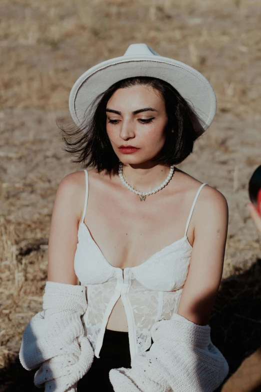 a beautiful woman in a white hat sits on the ground