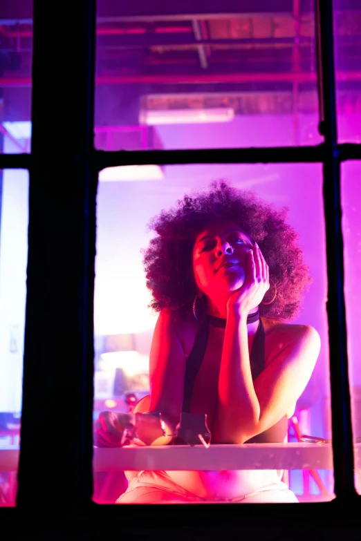 an african american woman with an afro sits in front of windows looking out at a group of people