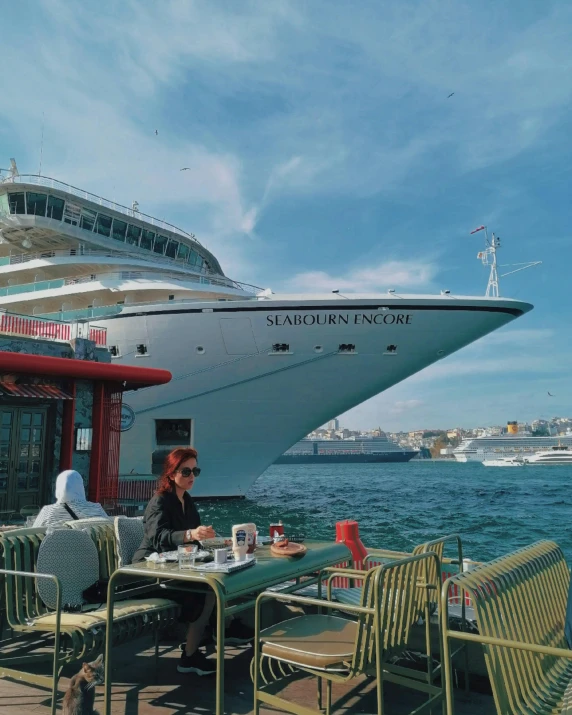 people are eating on the dock at an outdoor cafe near a cruise ship