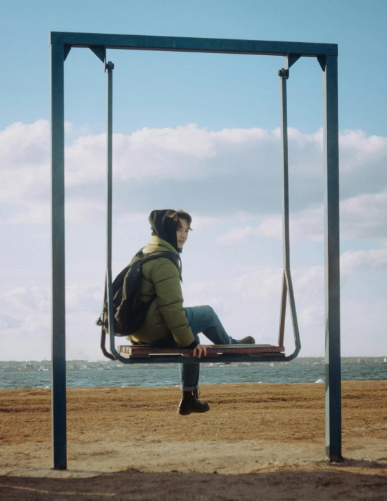 a man is sitting on a swing overlooking the ocean