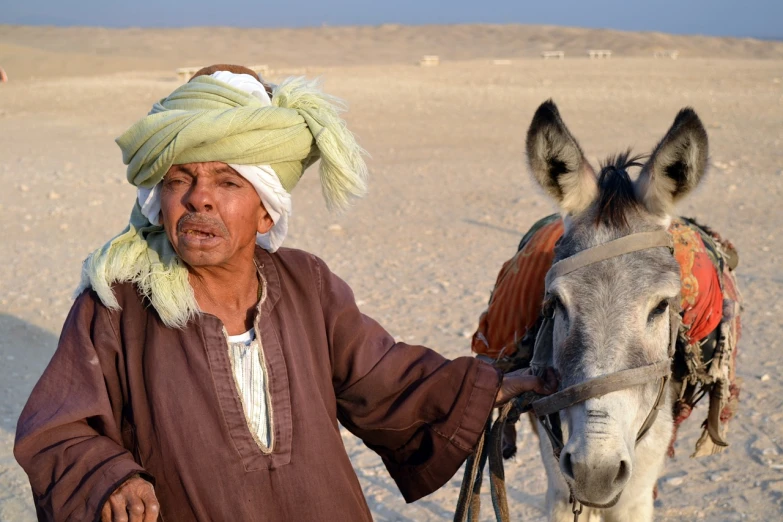 a man in a turban standing next to a donkey, by Robert Brackman, pexels, dau-al-set, egypt, afp, sand desert, two old people