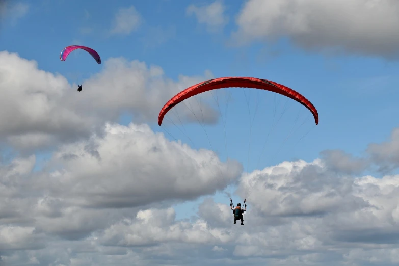 a couple of people that are parasailing in the sky, a picture, by Alison Watt, red cumulonimbus clouds, mundy, panorama, open wings