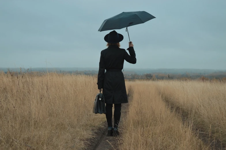 a woman walking down a dirt road holding an umbrella, pexels, conceptual art, black stetson and coat, in a field, sergey krasovskiy, walking to work with a briefcase