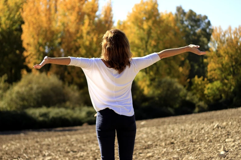 a woman standing in a field with her arms outstretched, a picture, pexels, figuration libre, autum, relaxed posture, simple, wearing a white sweater