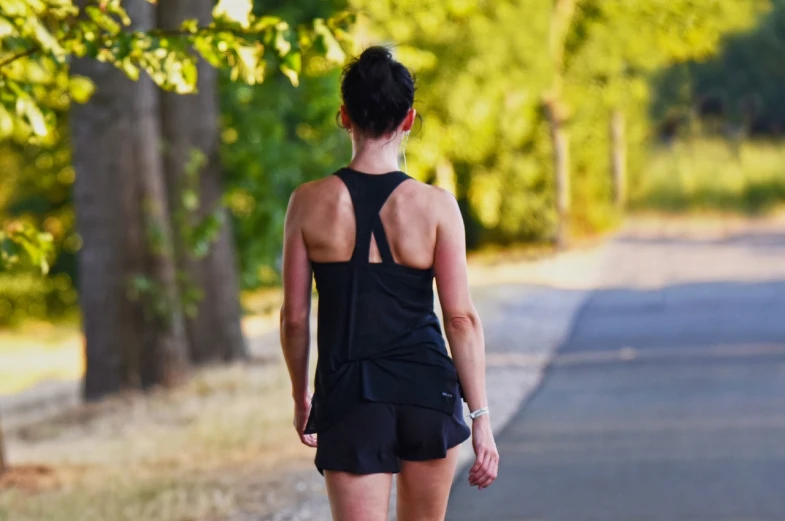 a woman riding a skateboard down a street, a picture, by Mathias Kollros, pexels, figuration libre, tight black tank top and shorts, walking in forest, 3 / 4 view from back, morning sun