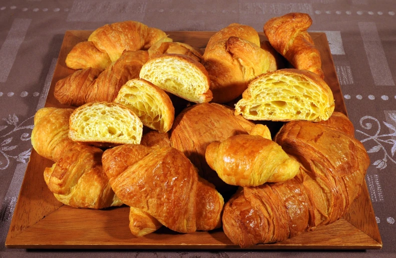 a wooden tray filled with croissants on top of a table, by Juan O'Gorman, yellow, various sizes, grain”, panini