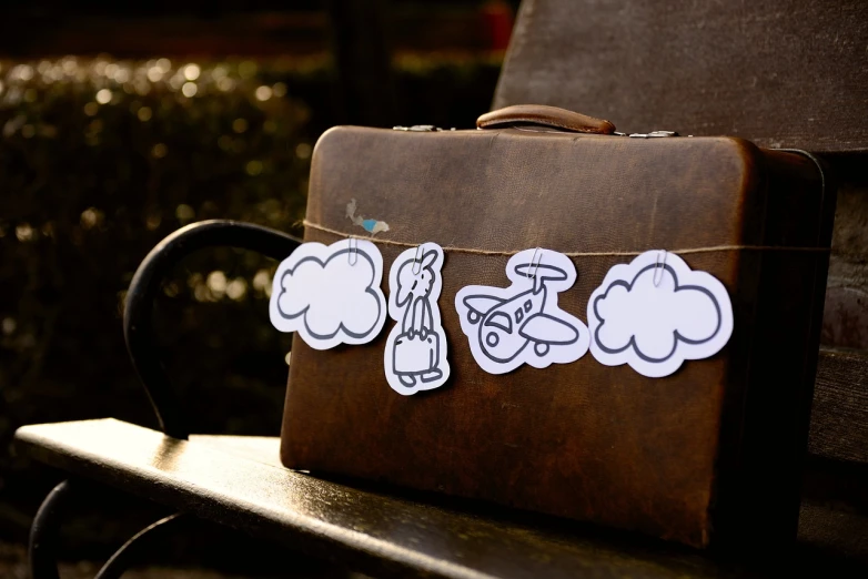 a suitcase sitting on top of a wooden bench, a picture, by Dóra Keresztes, paper decoration, clouds in the background, etsy stickers, stick figures