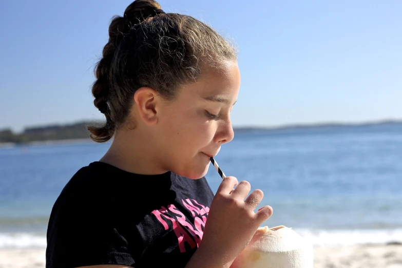 a girl drinking out of a coconut drink on the beach, a portrait, by David Garner, pixabay, sydney, aged 13, eating ice cream, profile shot