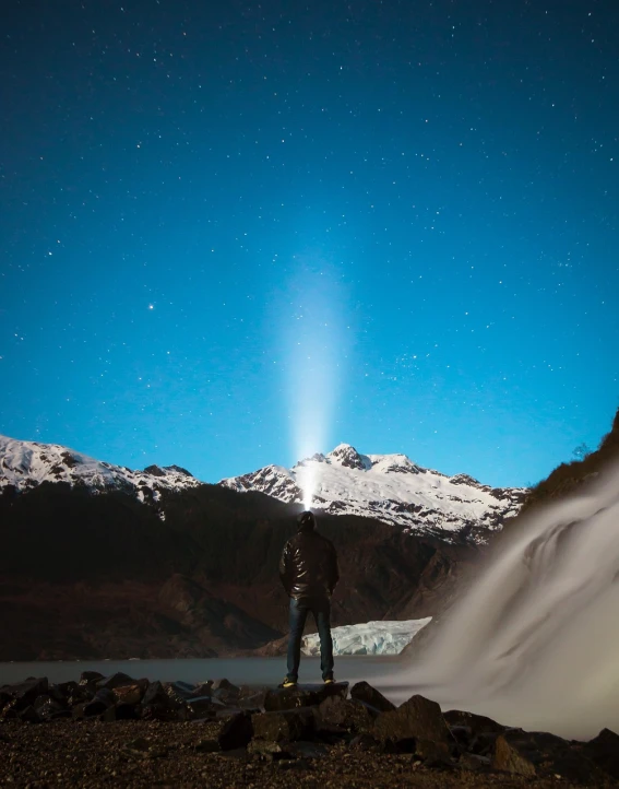 a man standing on top of a snow covered mountain, visual art, bioluminescent waterfall, singular light source from below, with a snowy mountain and ice, star in the sky