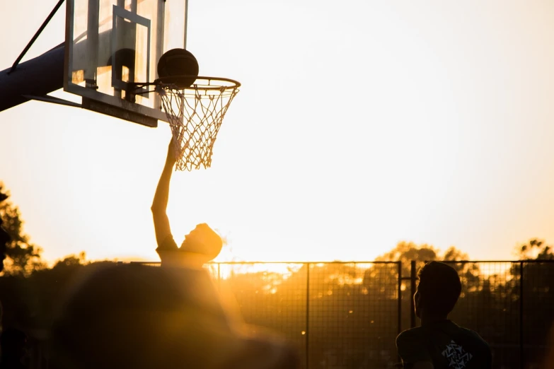 a man standing on top of a basketball court holding a basketball, a picture, by Matija Jama, pexels contest winner, blocking the sun, late summer evening, profile shot, dunking