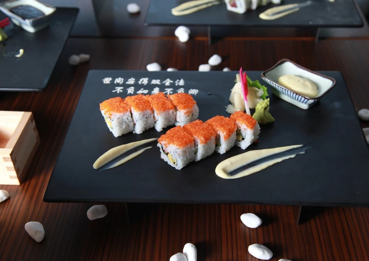 a black plate topped with sushi on top of a wooden table, a picture, high detail product photo