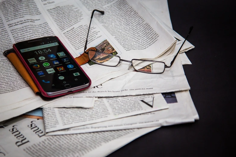 a cell phone sitting on top of a pile of newspapers, a picture, with glasses, gazeta, cell phone photo