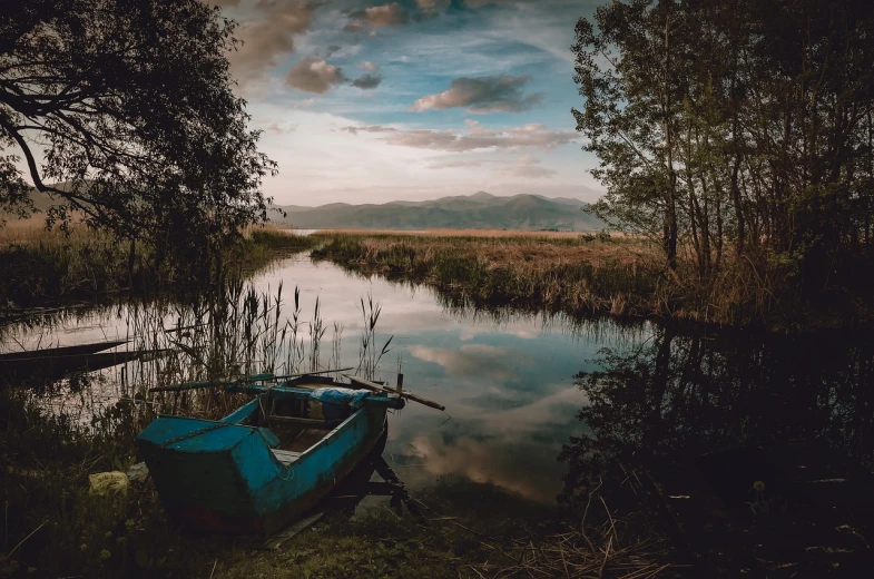 a blue boat sitting on top of a lake next to a forest, a picture, by Adam Szentpétery, pixabay, romanticism, on a dark swampy bsttlefield, overlooking river aufidius italy, fishing boat, in a vast serene landscape