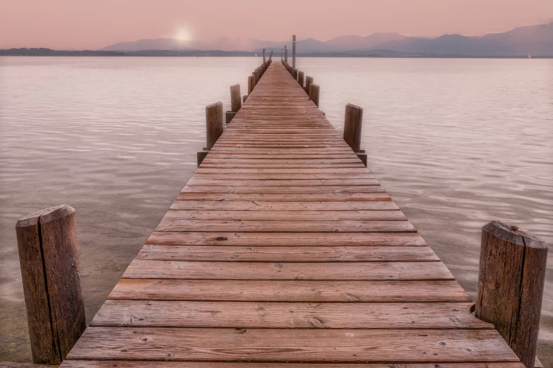 a wooden pier stretching out into the water, inspired by Jan Kupecký, romanticism, distant mountains lights photo, new mexico, hdr photo, the sky is a faint misty red hue