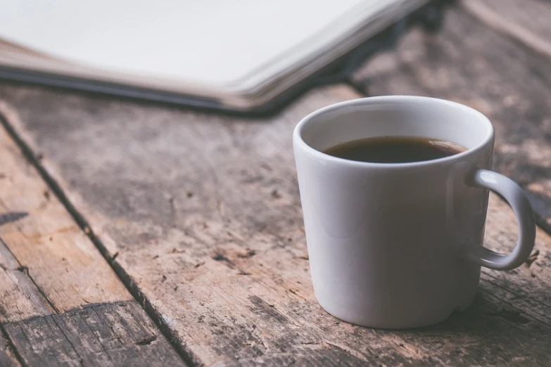 a cup of coffee sitting on top of a wooden table, a picture, by Karl Buesgen, unsplash, banner, uncluttered, empty, irregular