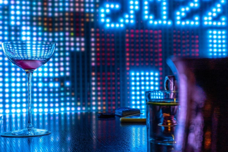 a wine glass sitting on top of a wooden table, a stock photo, cyberpunk nightclub, brightly lit blue room, neon electronic signs, robb cobb