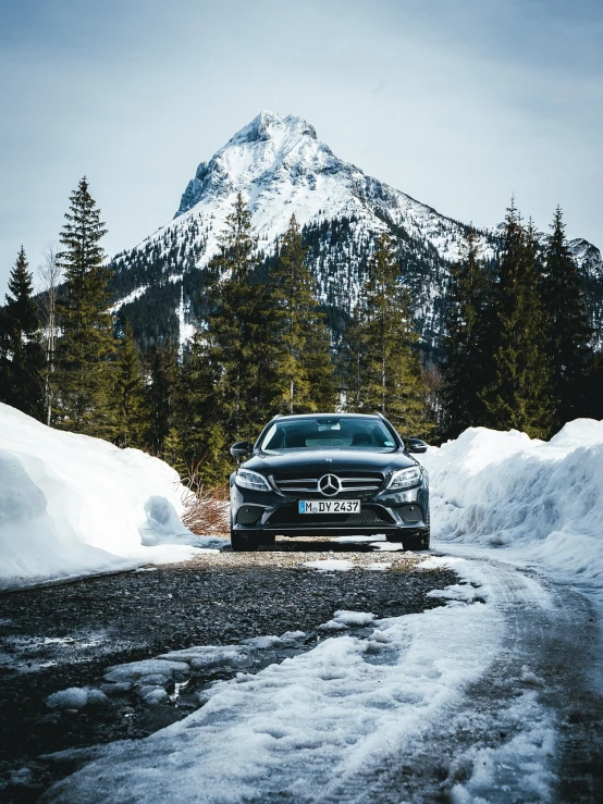 a car parked on a snowy road in front of a mountain, a picture, by Matthias Weischer, frontal pose, mercedez benz, black forest, low quality photo