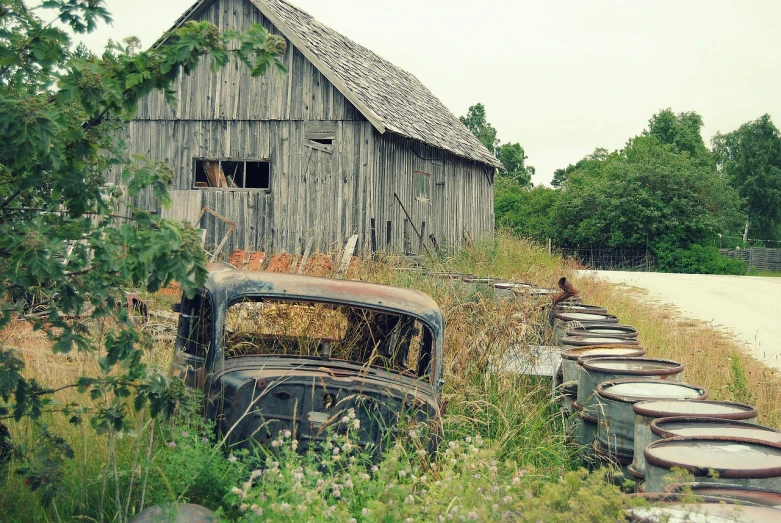 an old truck parked in front of a barn, flickr, folk art, old abandoned car sinking, a wide shot, an overgrown, wooden structures