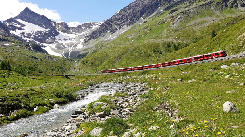 a red train traveling through a lush green valley, a photo, by Werner Andermatt, summer 2016, european river, very attractive, glacier