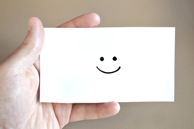 a hand holding a piece of paper with a smiley face drawn on it, minimalism, compressed jpeg, istockphoto, business card, happiness