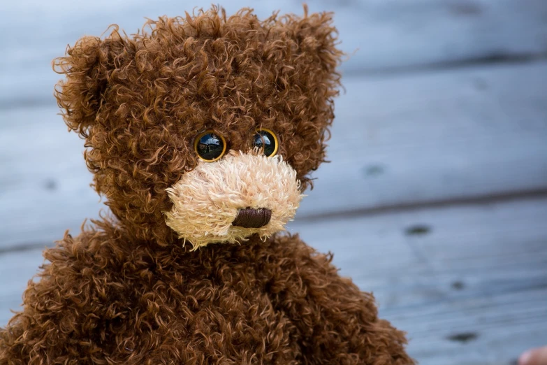 a brown teddy bear sitting on top of a wooden floor, inspired by Sam Havadtoy, pexels, process art, brown hair and large eyes, shaggy brown hair, amigurumi, up close picture