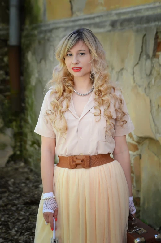 a woman standing in front of a wall holding a suitcase, a portrait, inspired by Alexis Simon Belle, flickr, long blond drill curls, pleated skirt, peach, wear's beige shirt