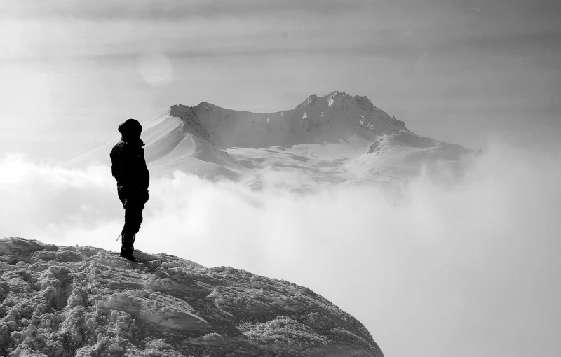 a person standing on top of a snow covered mountain, a black and white photo, by Andrei Kolkoutine, fog mads berg, visible from afar!!, profile perspective, screensaver