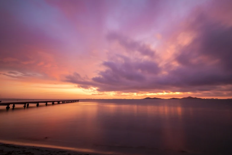 a large body of water under a cloudy sky, a picture, unsplash, purple orange colors, near a jetty, vibrant sunrise, okinawa japan