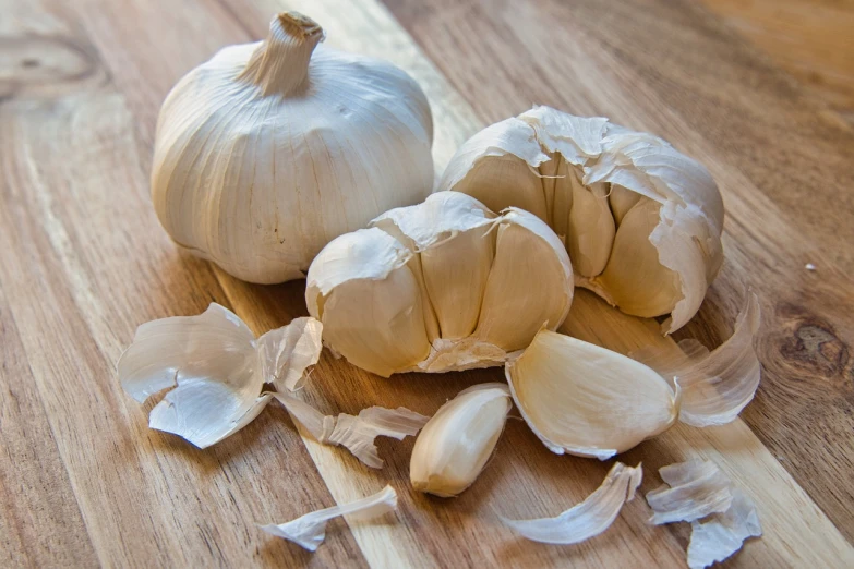 a couple of garlic cloves sitting on top of a wooden table, a picture, by Paul Emmert, shutterstock, mangled, white haired, close-up product photo, snacks