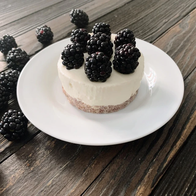 a white plate topped with a cake covered in blackberries, by Emma Andijewska, pexels, on a wooden plate, yogurt, 7 0 mm photo, stock photo