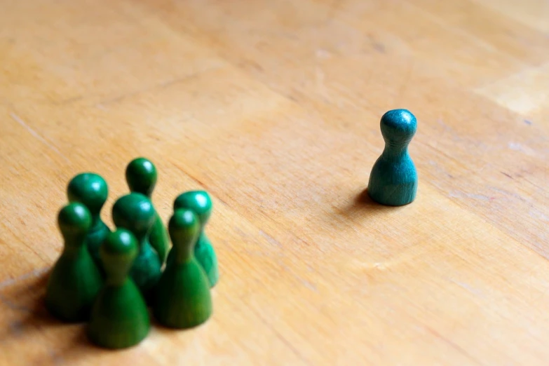 a group of green figurines sitting on top of a wooden table, a picture, unsplash, figurativism, standoff, a person standing in front of a, matching colors, on a wooden plate