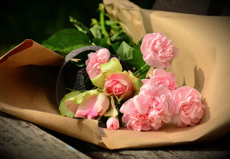 a bunch of pink roses sitting on top of a wooden bench, a picture, by Maksimilijan Vanka, pixabay, cardboard, wrapped in flowers, : 5 stylish, draped in fleshy green and pink