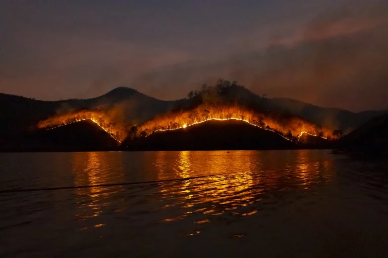 a large body of water with a mountain in the background, the forest is on fire, evenly lit, stunning lines, bushfire